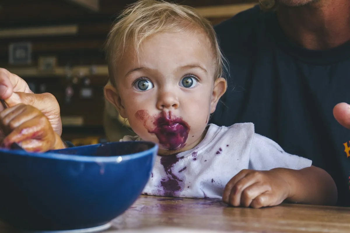 A toddler eating from a blue bowl at a table