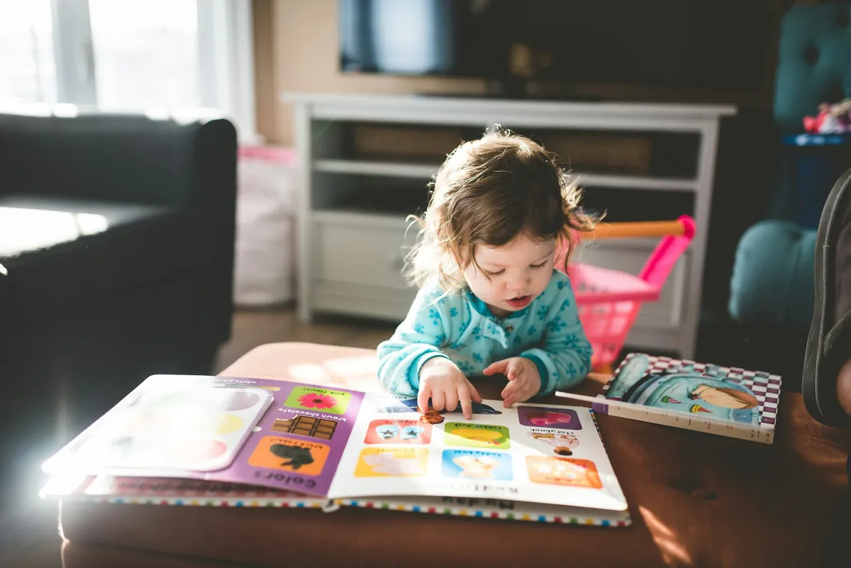A toddler sitting on the floor looking at a picture book