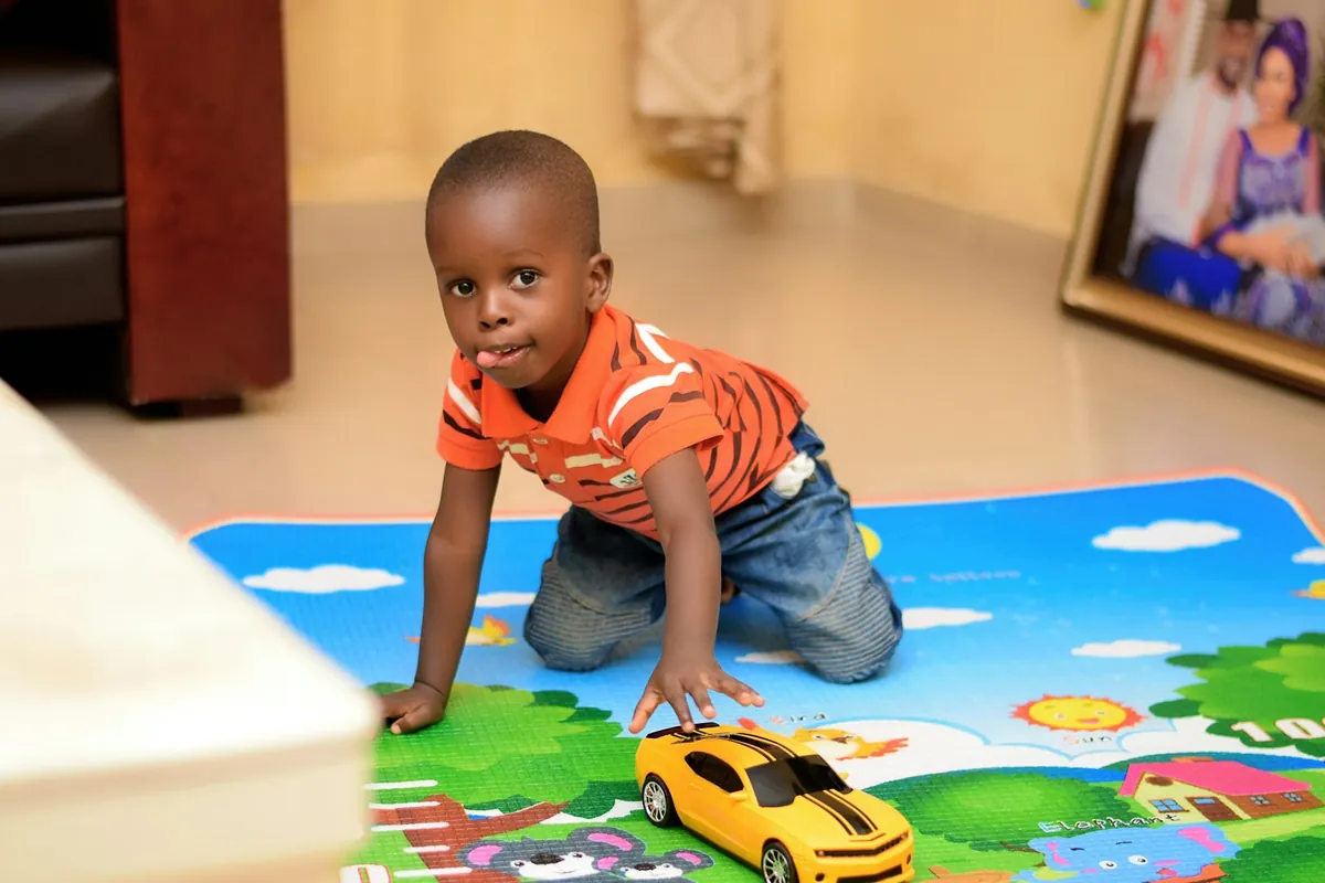 A toddler playing with a toy car on a colourful play mat