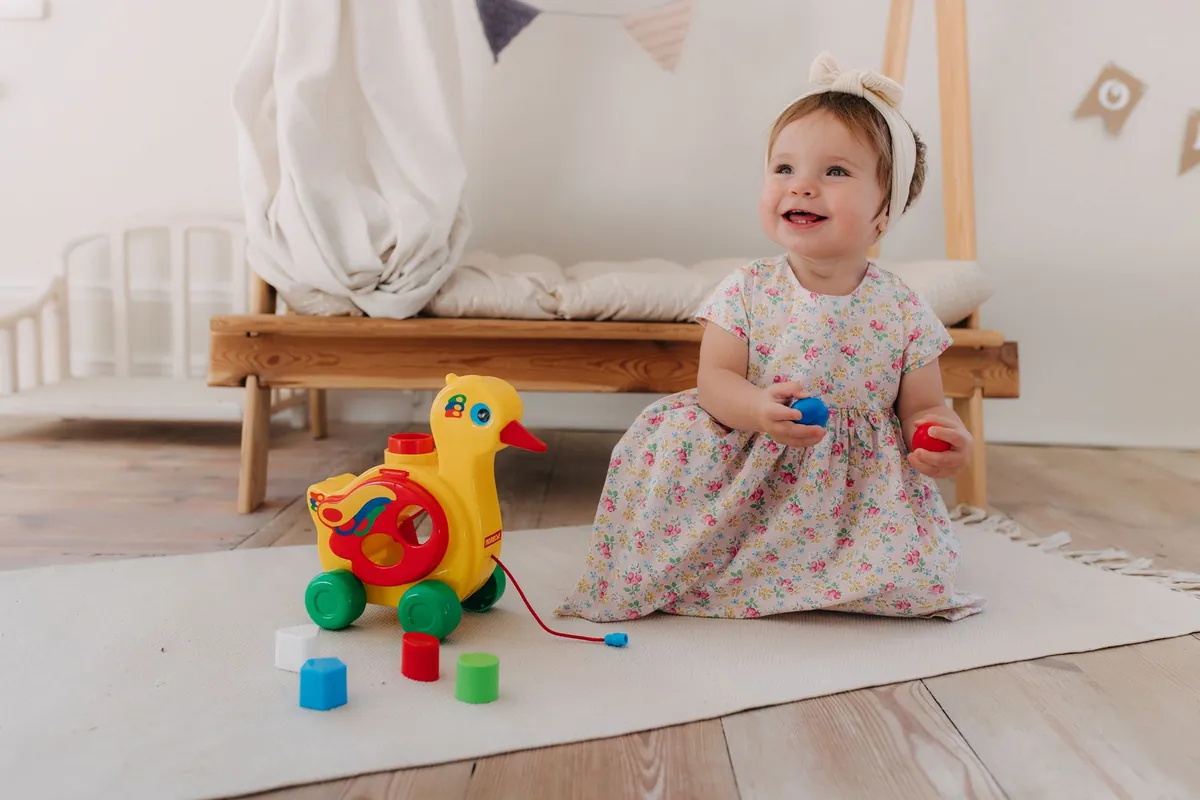 A toddler sitting on a rug with a wooden pull-along toy