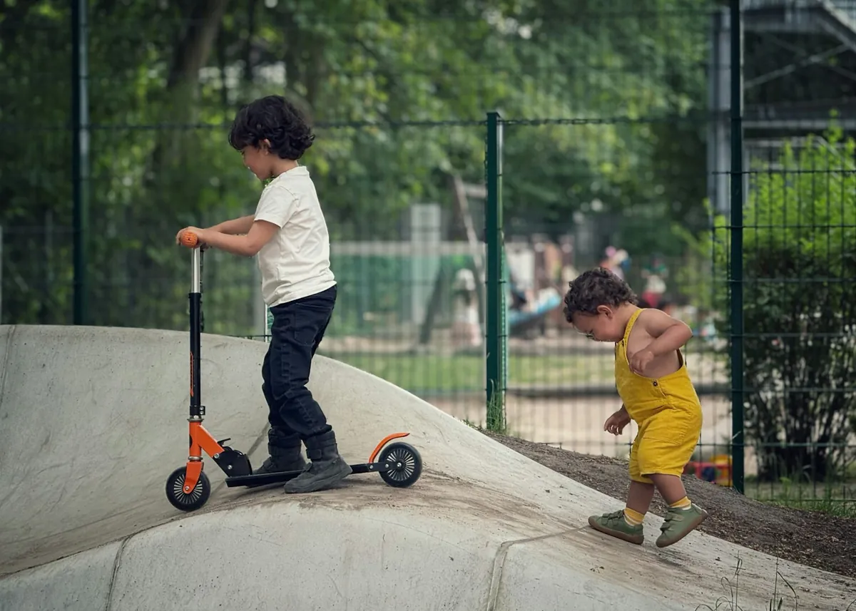 A young child riding a scooter while another child watches