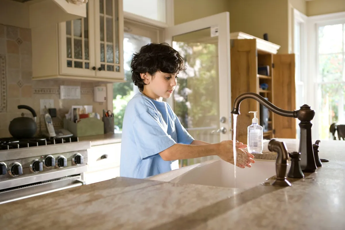 A young child rinsing their hands under a running tap