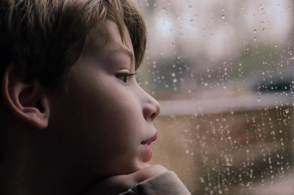 A young child watching raindrops run down a window