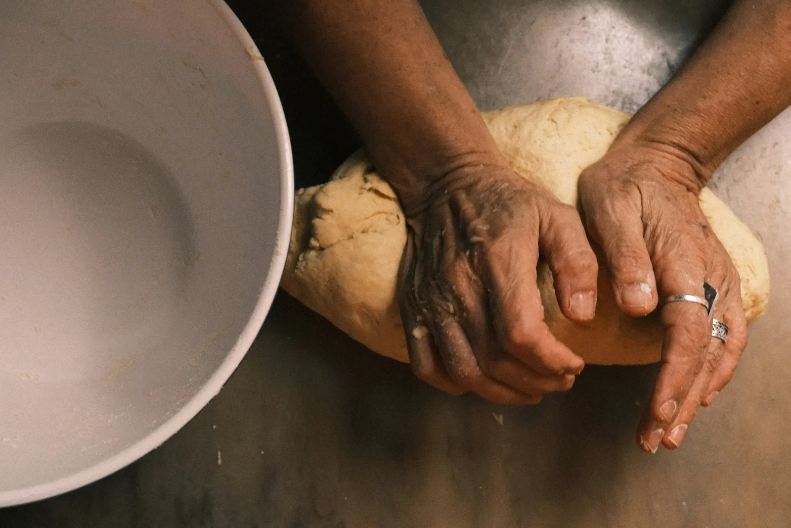 Two hands kneading dough beside a ceramic mixing bowl
