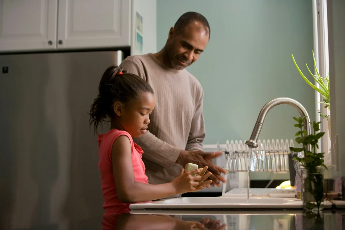 An adult and a child washing hands at a kitchen sink