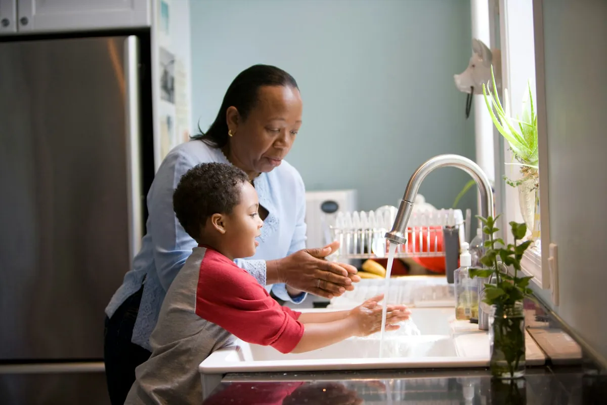 An adult helping a child wash their hands at a sink