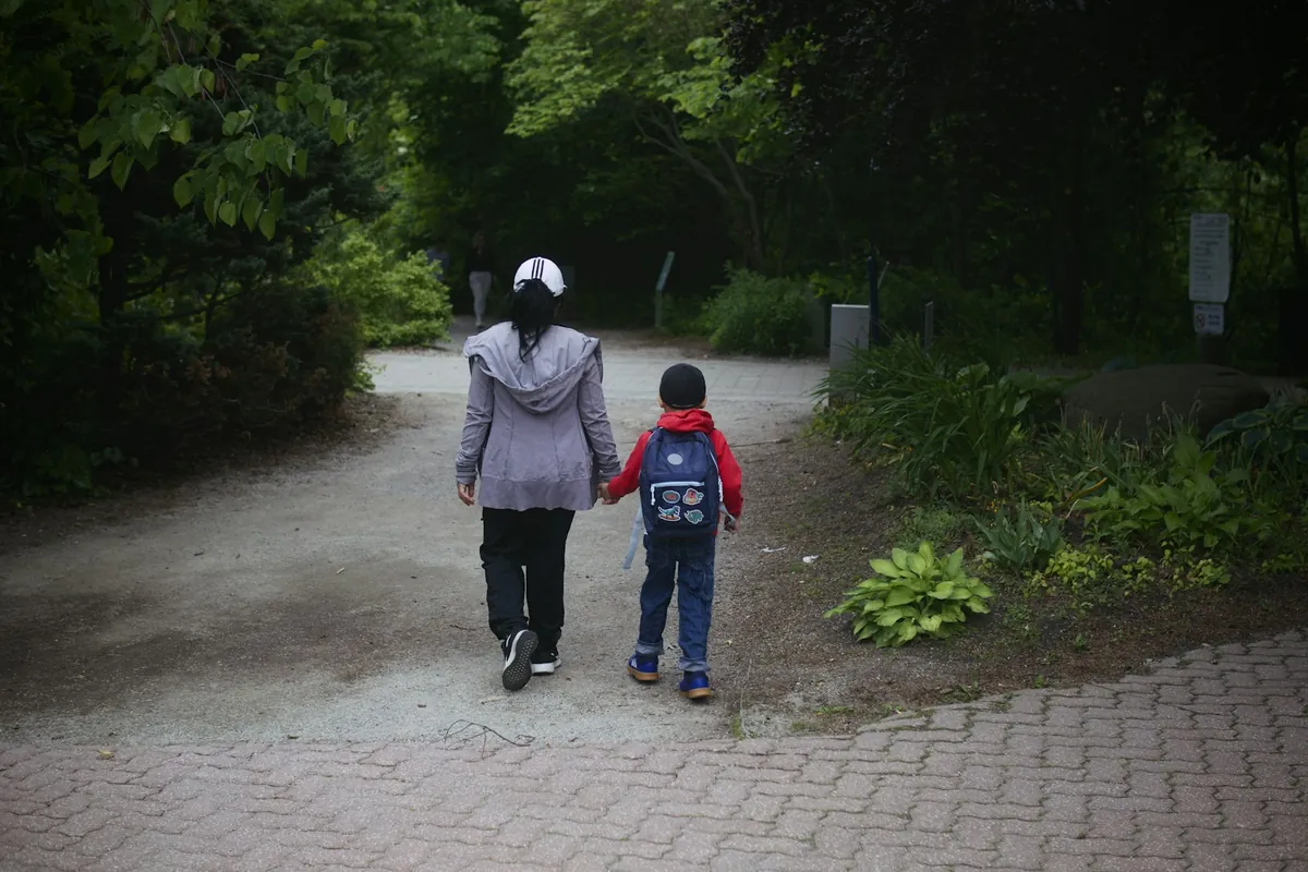 An adult and a child walking hand in hand along a park path