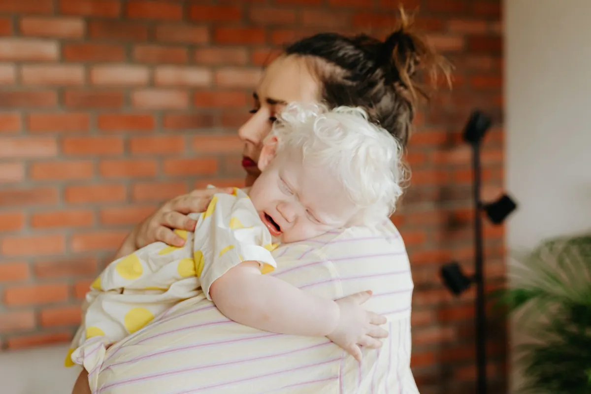 An adult comforting a small child against their shoulder