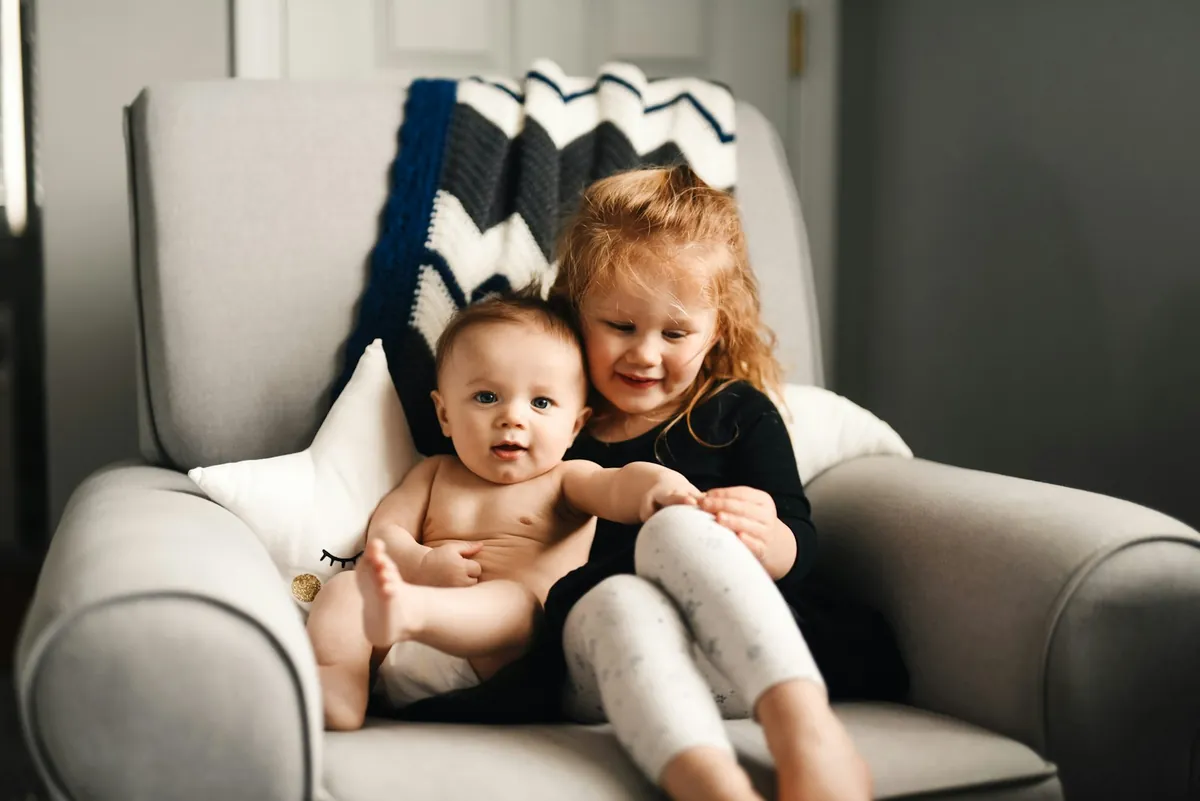 An older child sitting in a chair holding a baby