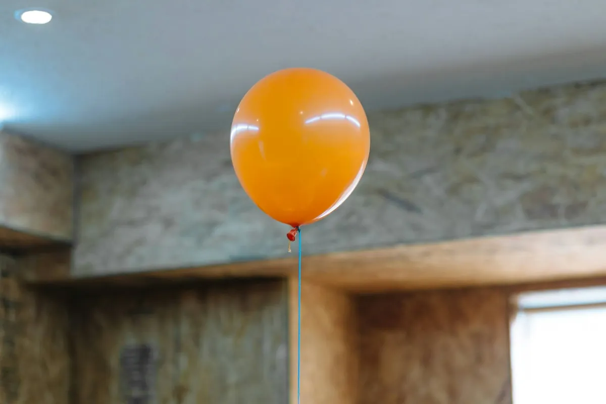 An orange balloon floating against a ceiling indoors