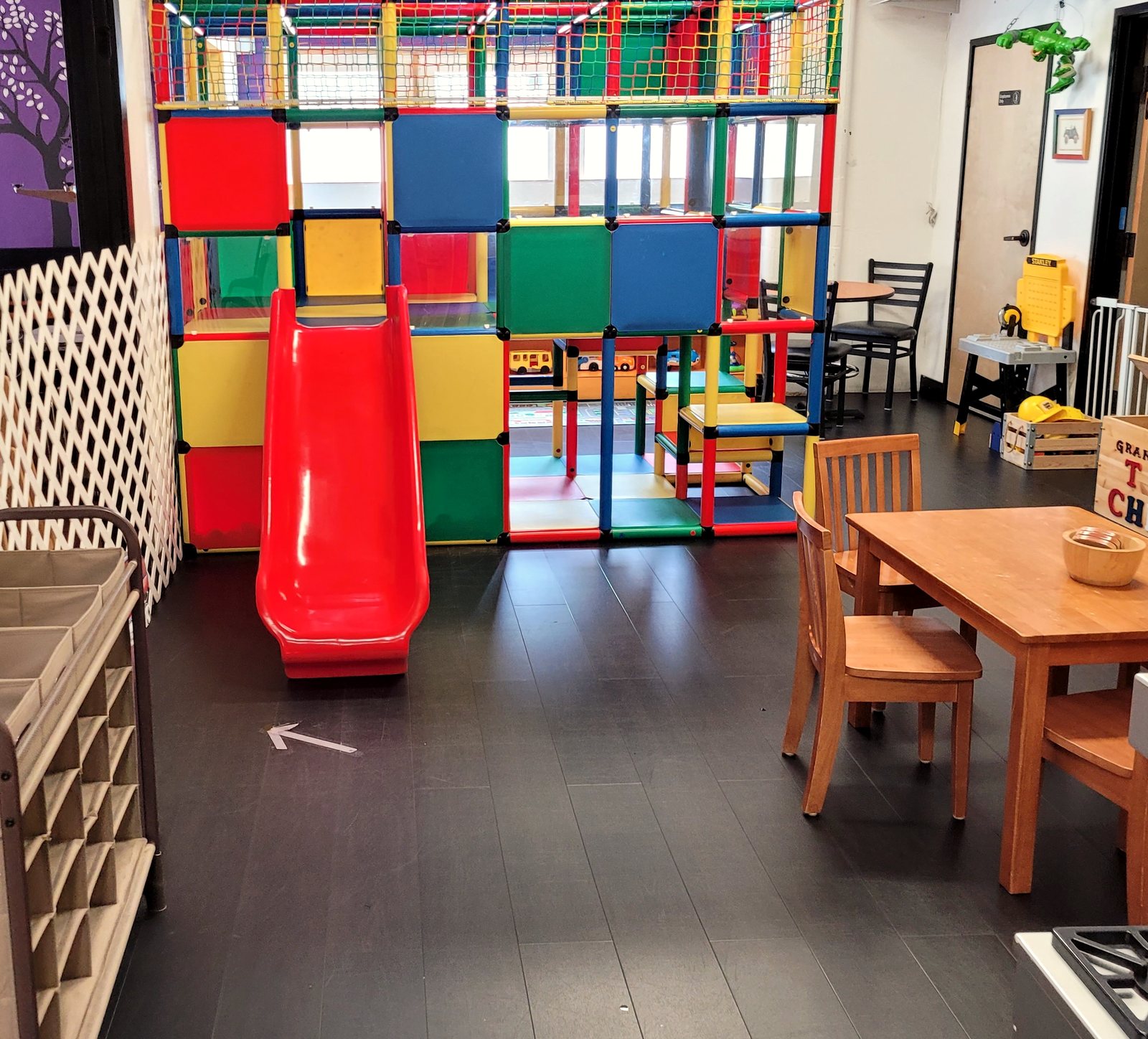 The playroom at Two Sisters Play Cafe, with a climbing structure, red slide and wooden tables