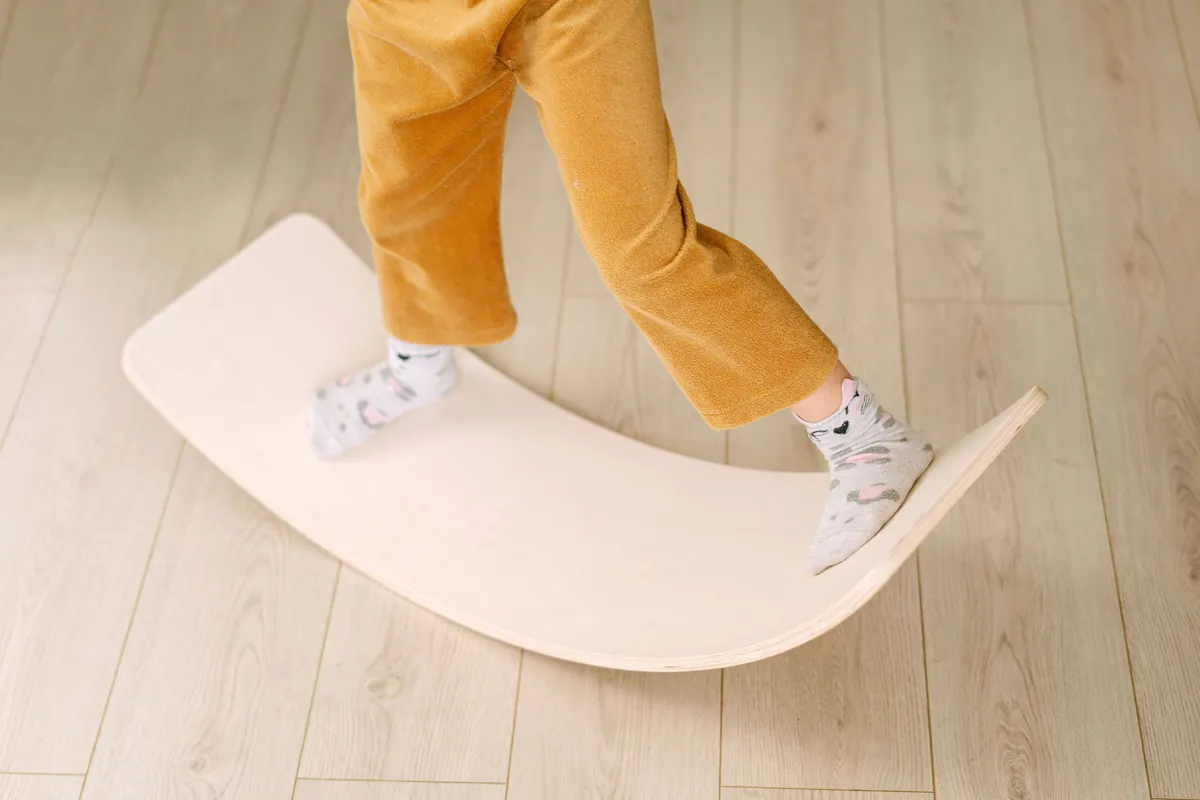 A child in socks balancing on a wooden board during indoor play