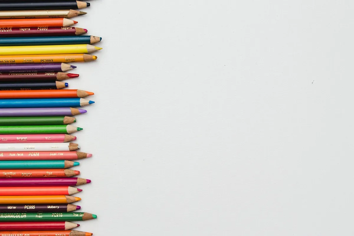 A row of coloured pencils beside a sheet of blank paper