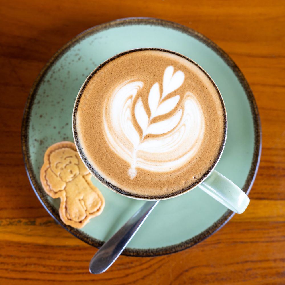 A latte with heart art in a sage-green cup on a wooden table