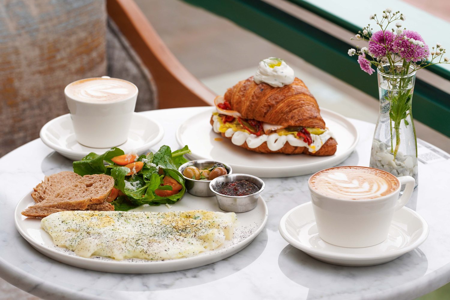 A cafe breakfast of a croissant sandwich and two lattes