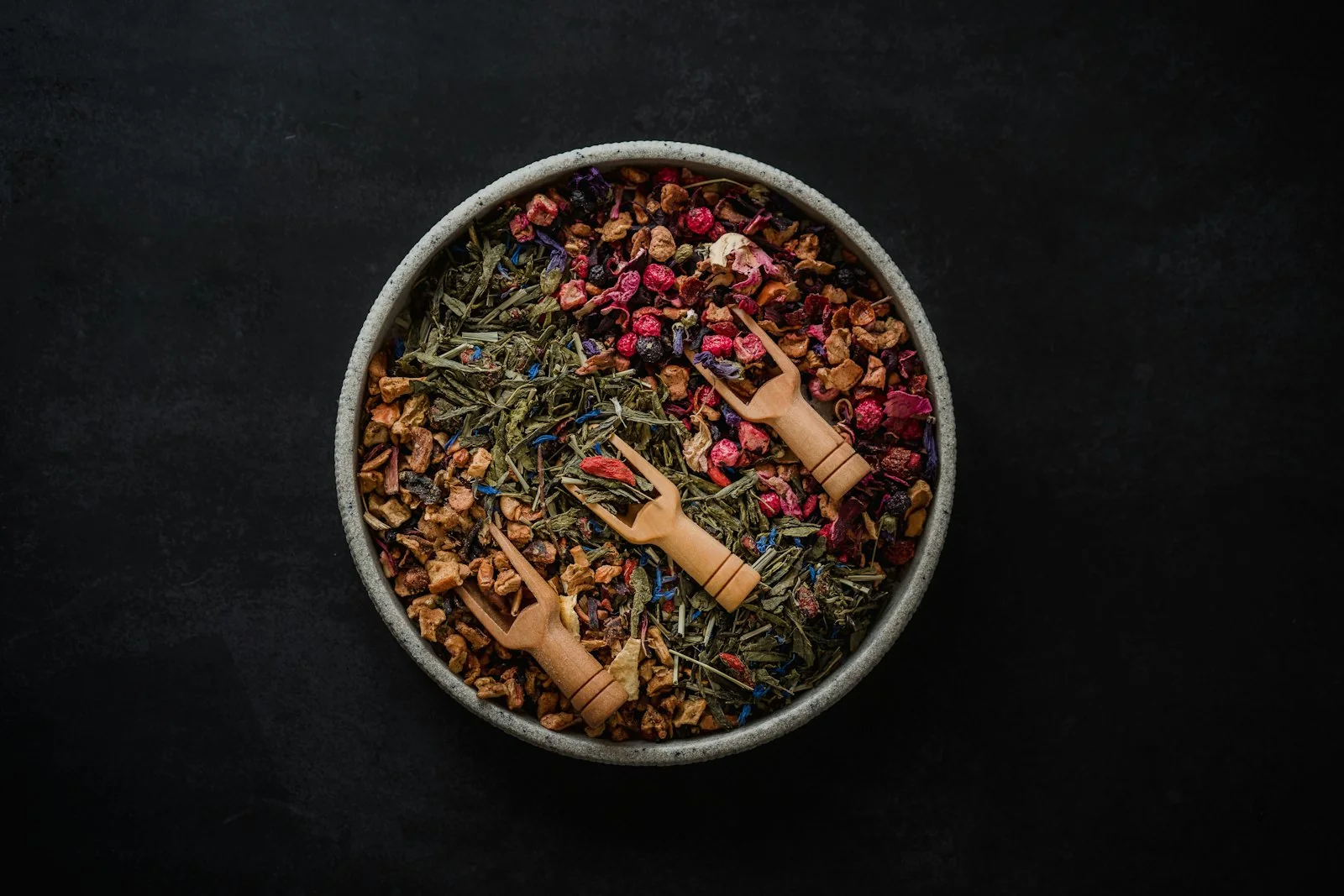 A dark bowl of loose leaf tea with dried petals and spices