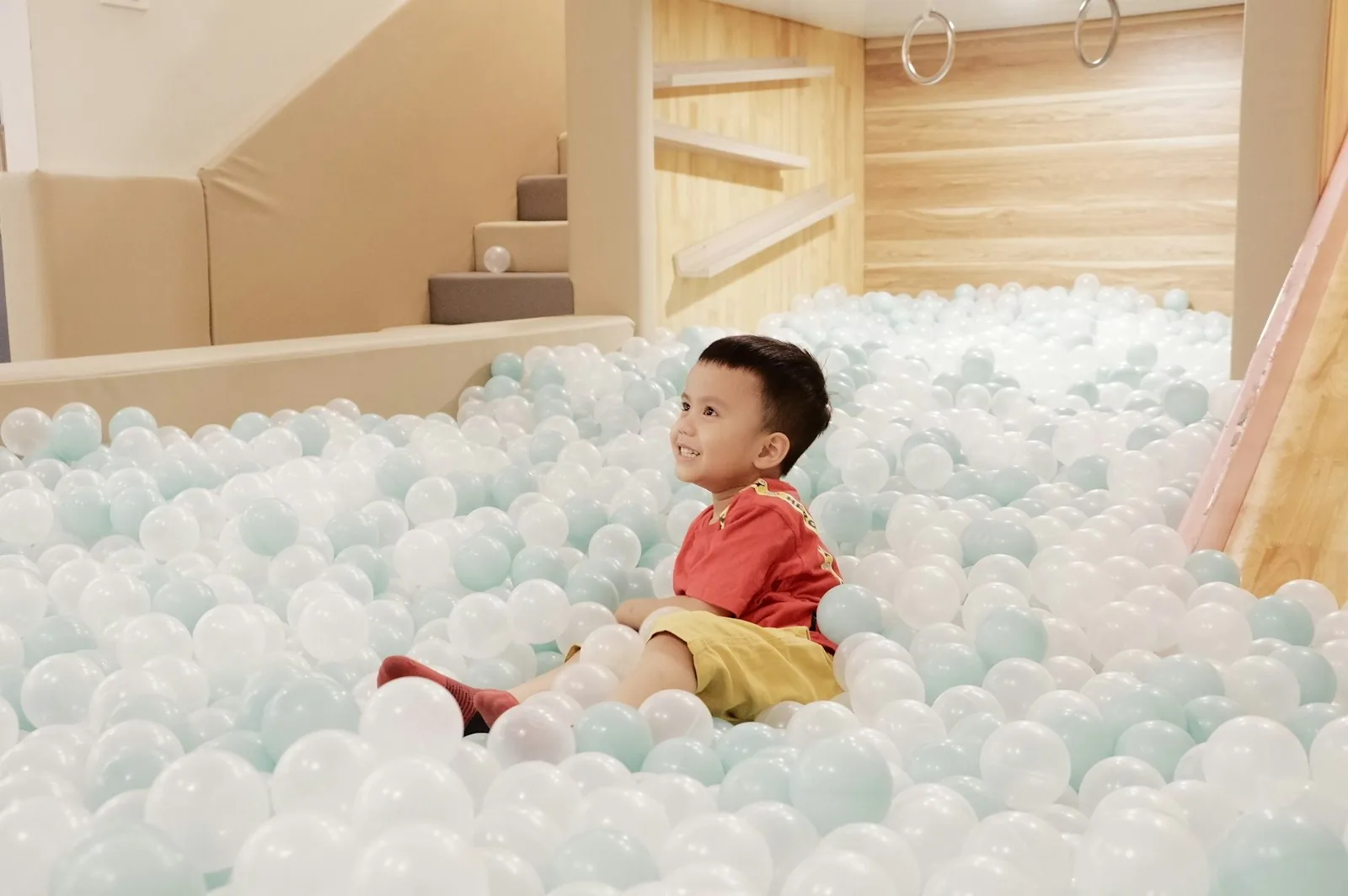 A young child sitting in a soft cream ball pit in a wooden play area