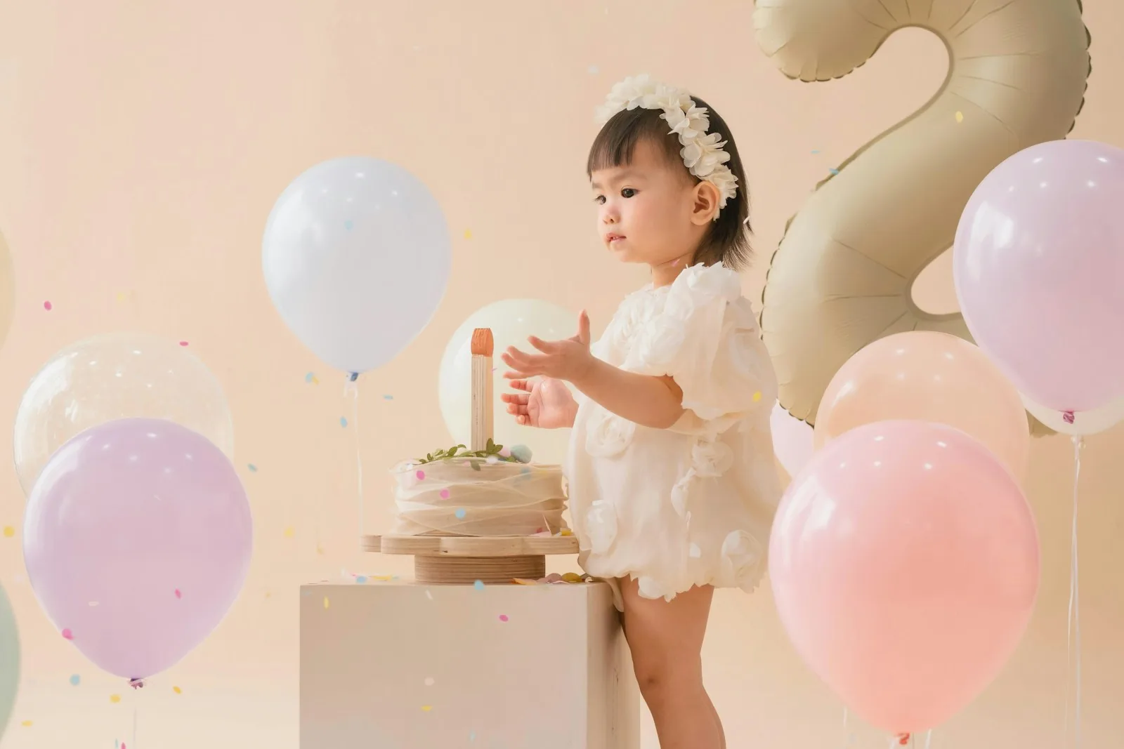 A small child beside a cake surrounded by pastel balloons