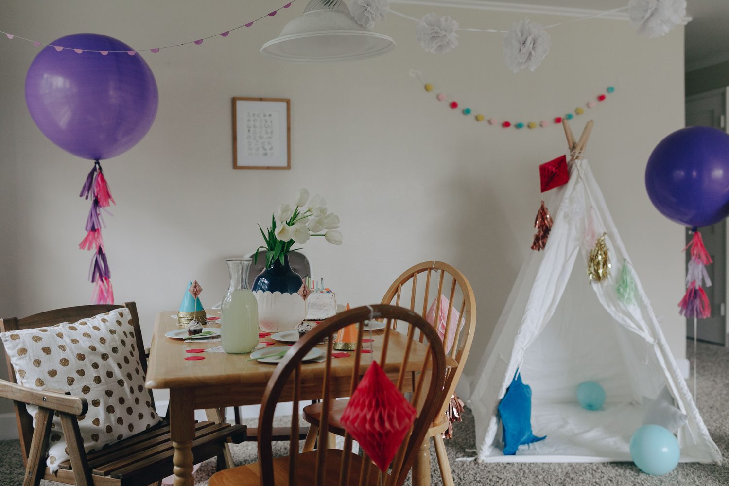 A calm birthday party set-up with balloons, a play teepee and a decorated table