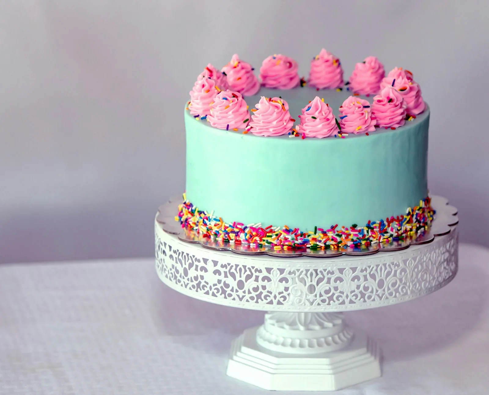 A pale iced birthday cake with piped swirls on a white cake stand