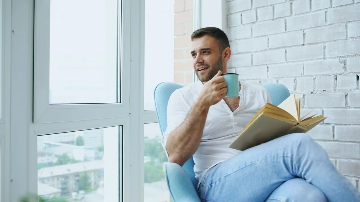 A person reading with a hot drink beside a bright window