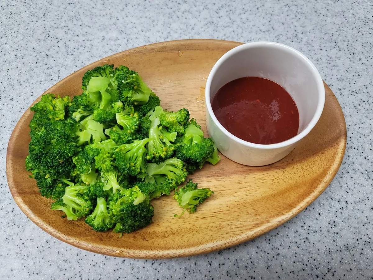 Steamed broccoli served on a wooden board with a dip