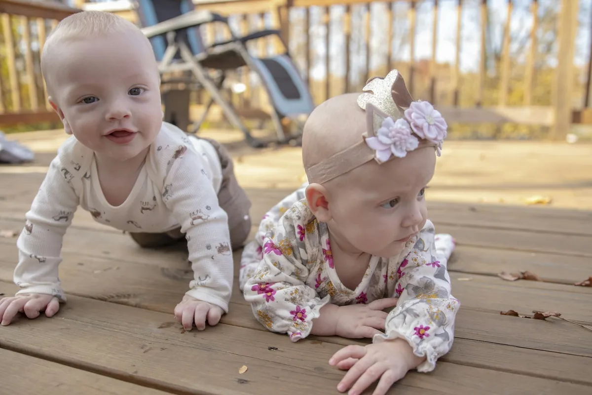 Two babies playing on a blanket on the floor