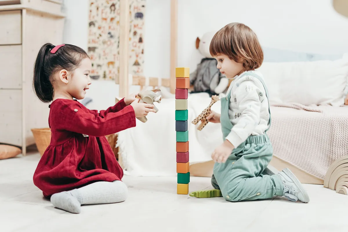 Two young children playing with stacking toys on a rug