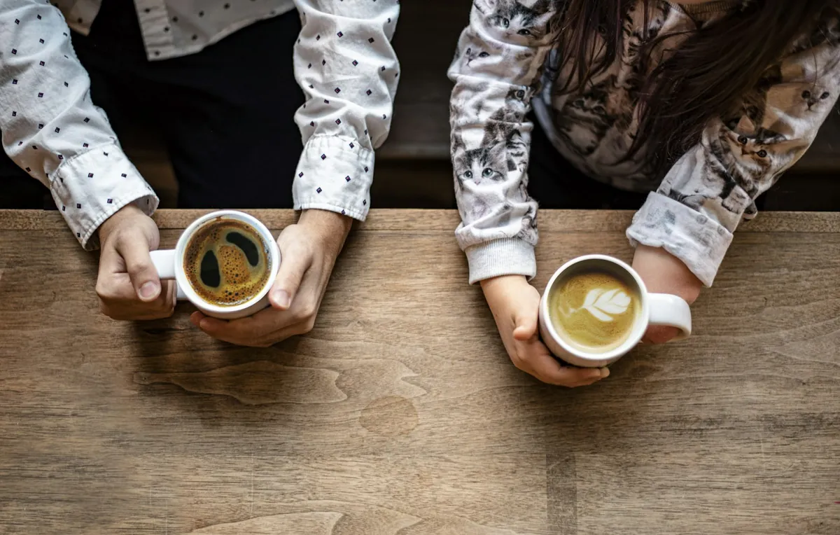 Two cups of coffee held over a wooden table