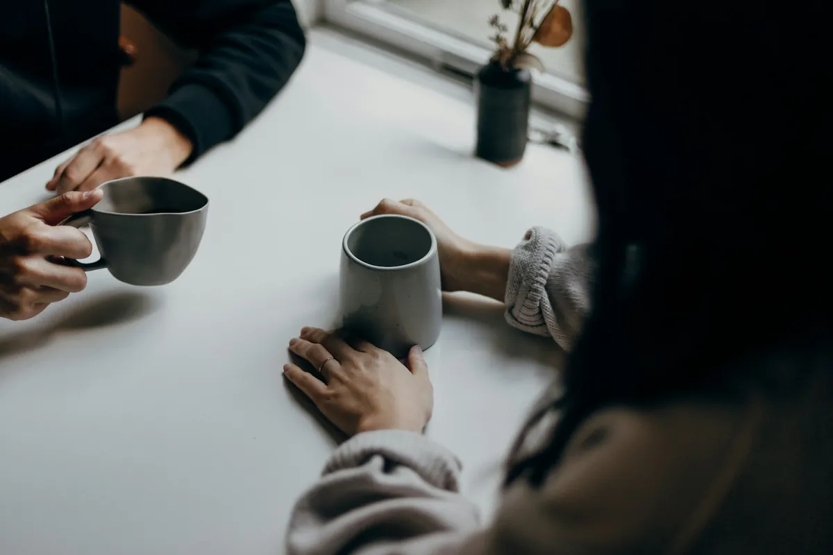 Two people holding mugs across a table