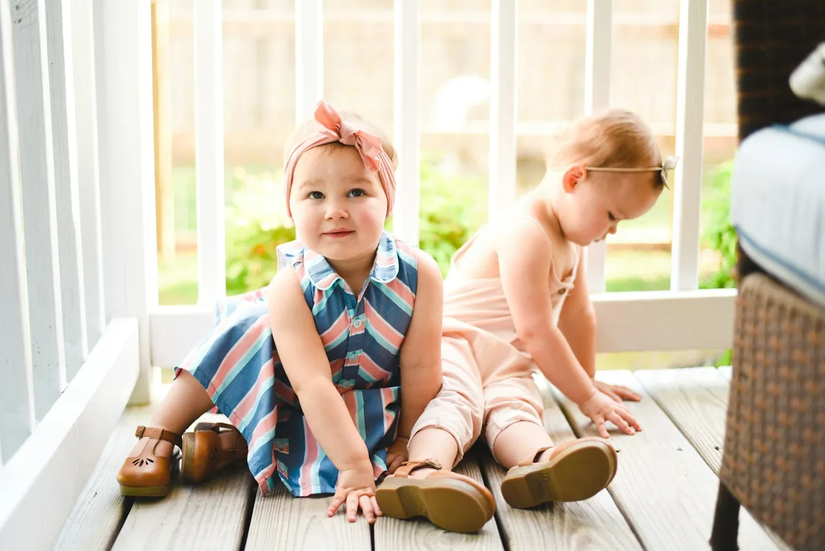 Two toddlers sitting together on the floor by a window