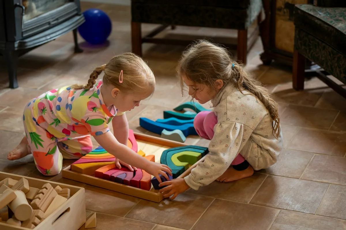 Two young children playing together with wooden toys on the floor